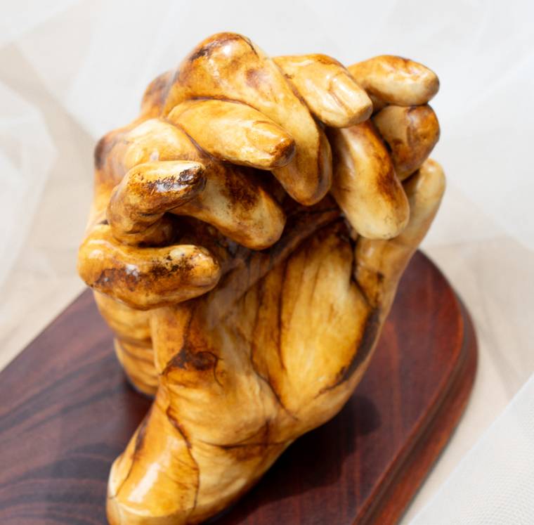 Escultura en yeso de dos manos entrelazadas sobre una base de madera.