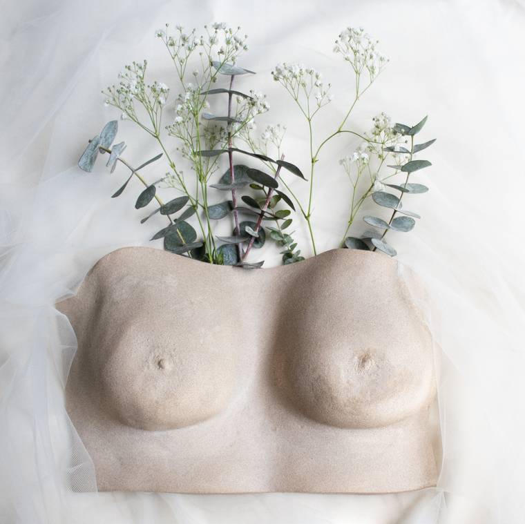 Escultura de pechos en yeso con acabado natural, rodeada de eucalipto.