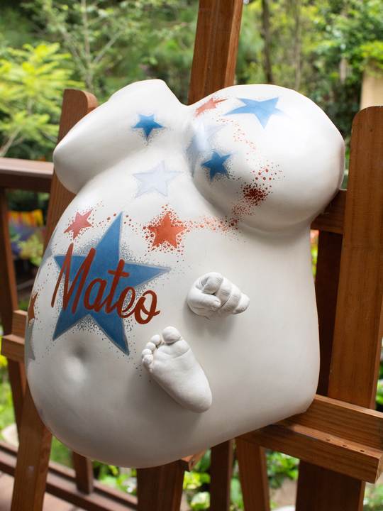 Barriga en yeso blanca con estrellas y las esculturas de la mano y el pie del bebé pegadas.